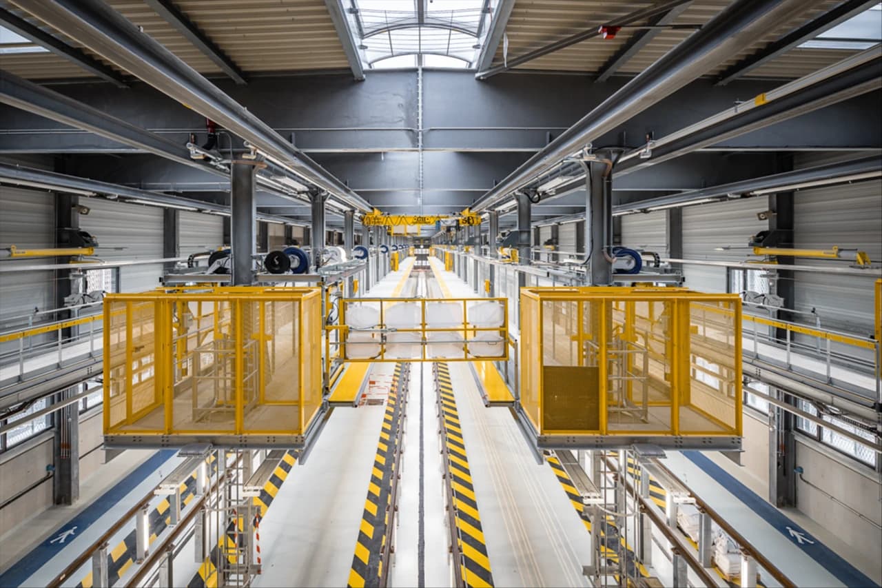Intérieur d’un atelier industriel moderne avec passerelles de maintenance jaunes, rails au sol et structures métalliques, éclairé par une verrière en toiture