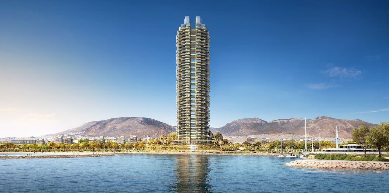 Un gratte-ciel élancé avec de nombreux balcons végétalisés s'élève majestueusement au bord de la mer, flanqué d'une promenade côtière verdoyante et de montagnes en arrière-plan sous un ciel bleu éclatant.