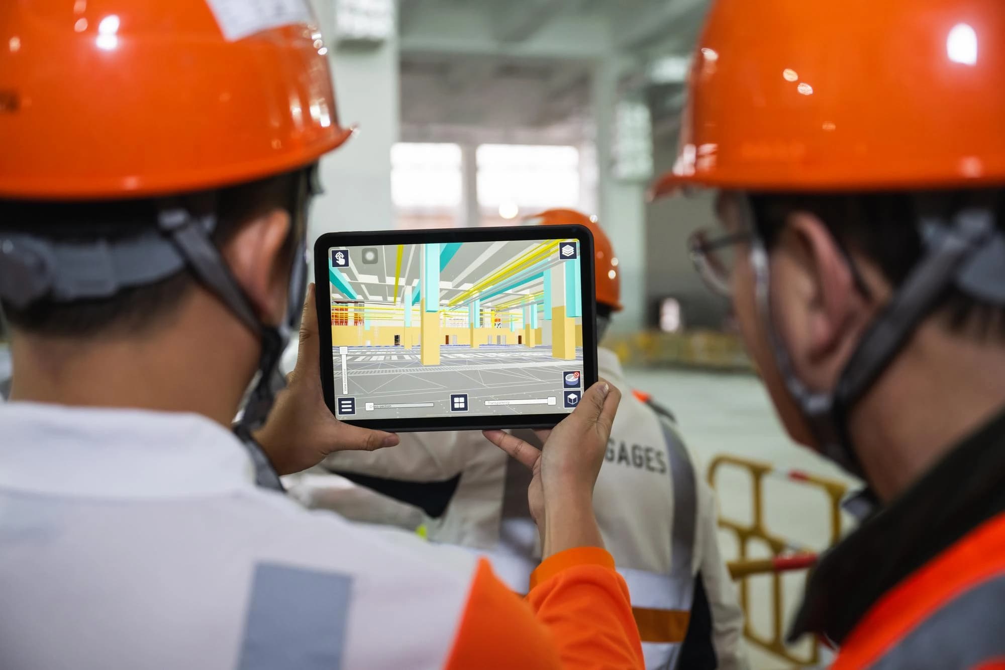 Deux ouvriers du bâtiment en casques orange regardent une tablette affichant un modèle BIM 3D coloré d'un intérieur de bâtiment, probablement pour la visualisation ou la planification sur site.