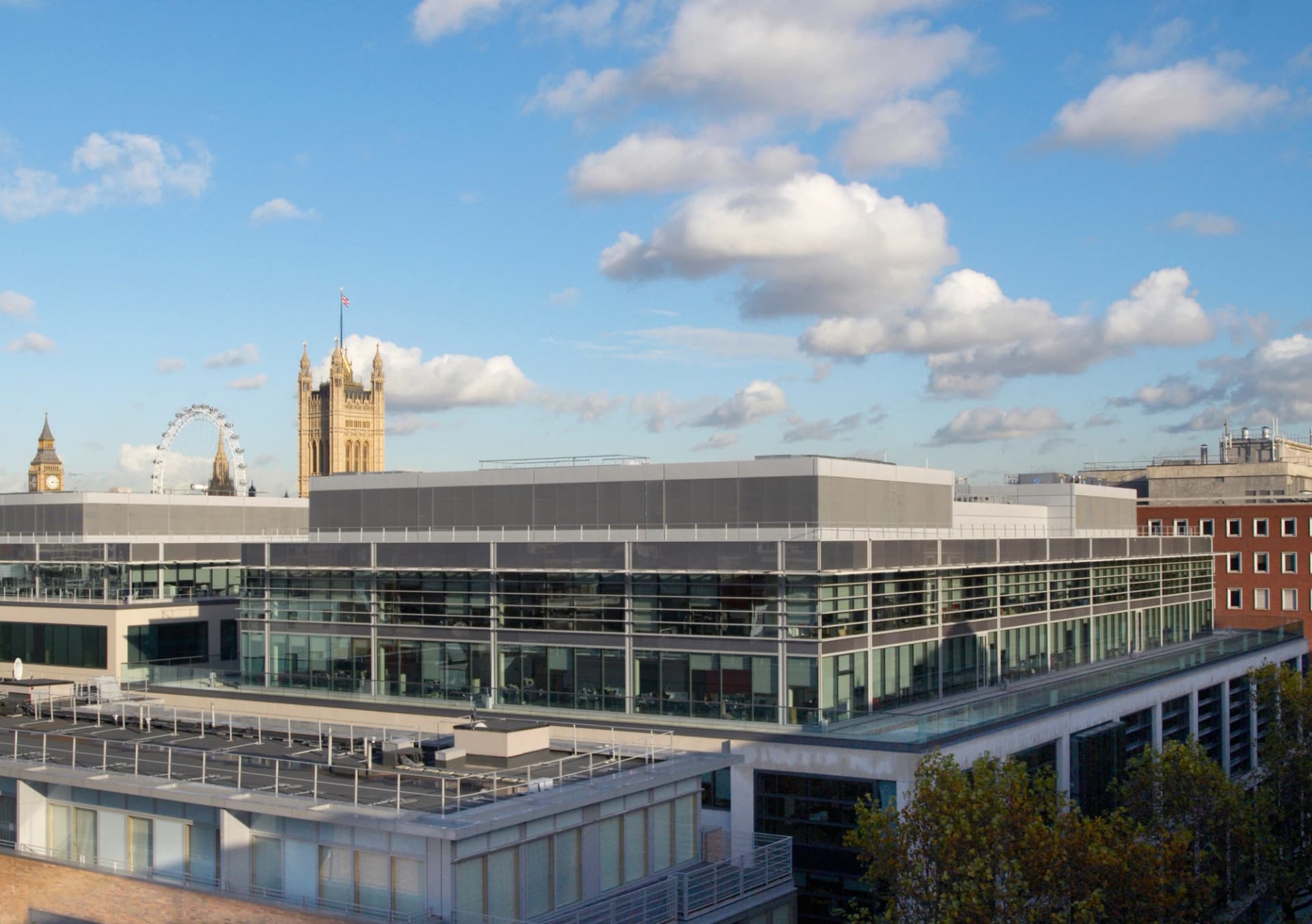 Toits de Londres avec bureaux modernes, Big Ben et le London Eye sous un ciel bleu parsemé de nuages blancs.