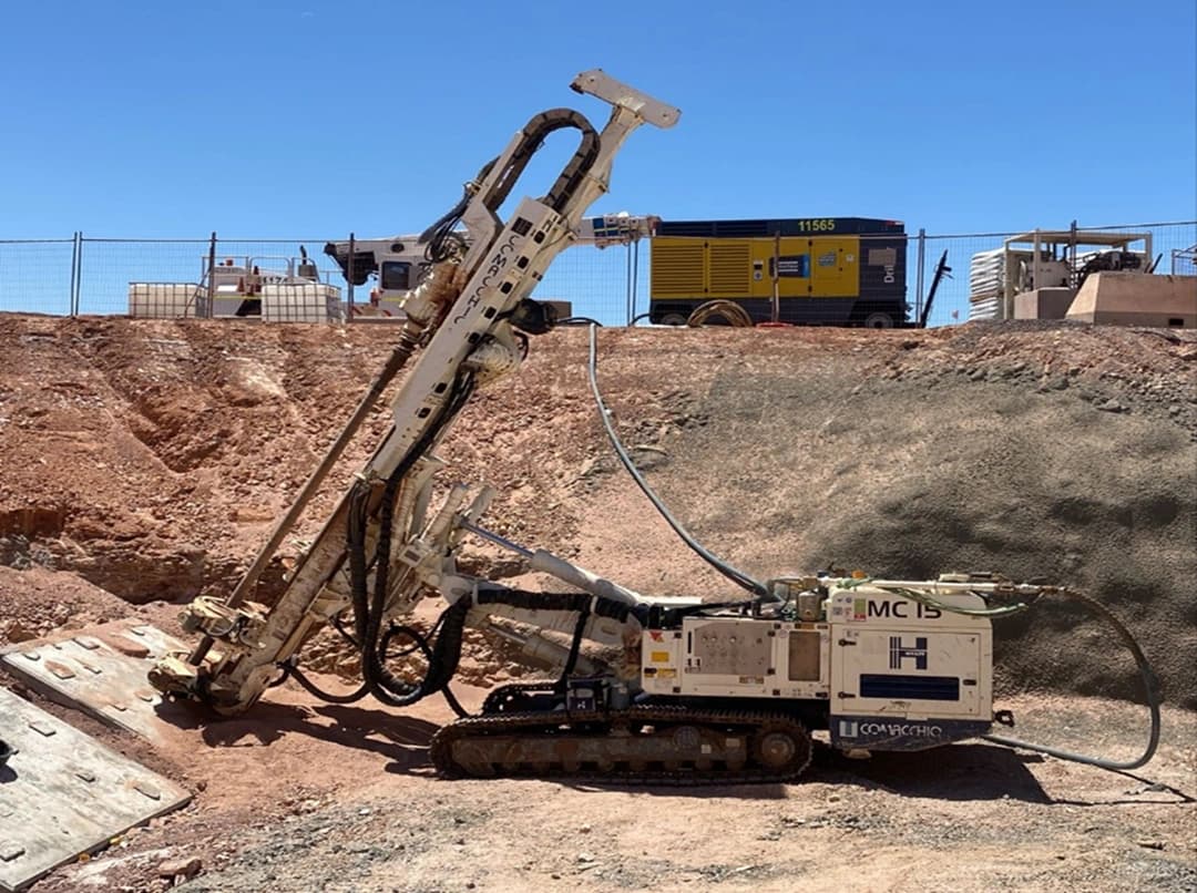 Une foreuse hydraulique Comacchio MC 15 sur chenilles en opération sur un chantier de construction ou minier.