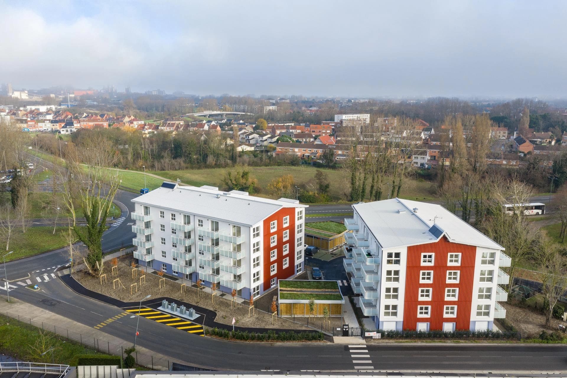 Vue aérienne de deux immeubles d'habitation modernes blancs et rouges dans une zone urbaine.