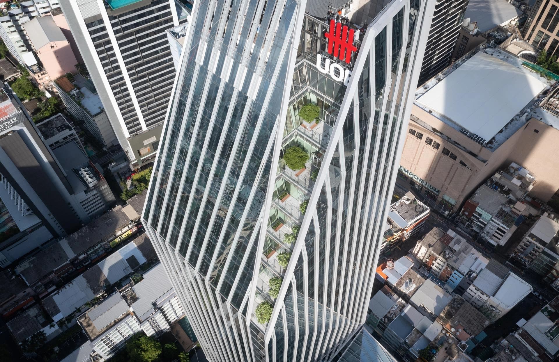 Vue aérienne d’une tour de bureaux contemporaine à façade vitrée avec lignes architecturales inclinées et terrasses végétalisées intégrées en milieu urbain.