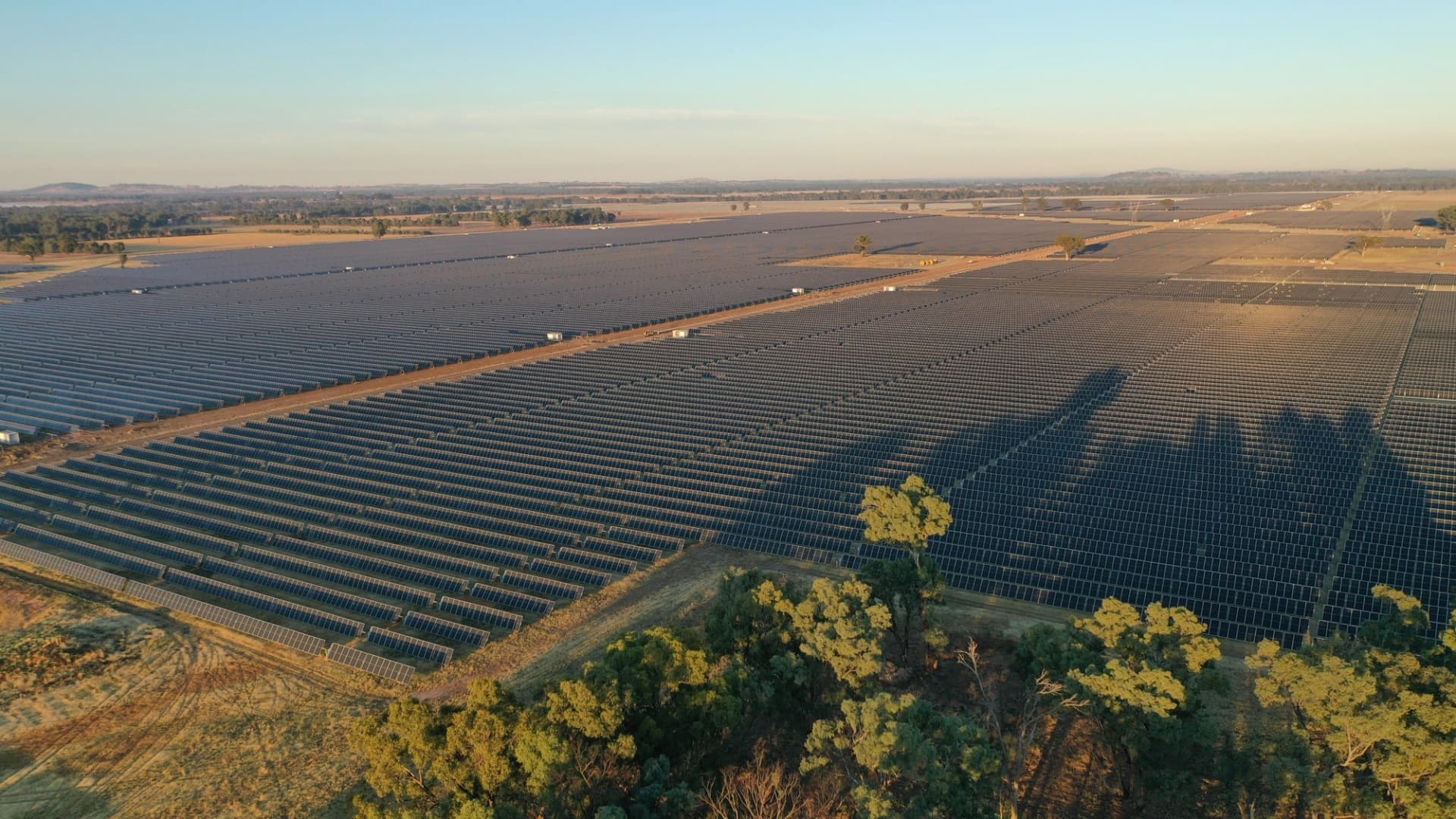 Vue aérienne d'un immense parc de panneaux solaires en milieu rural au coucher du soleil.