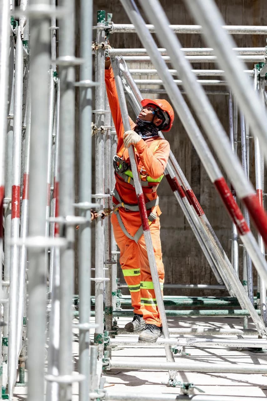 Un ouvrier du bâtiment en salopette orange et casque de sécurité, assemble un échafaudage métallique.