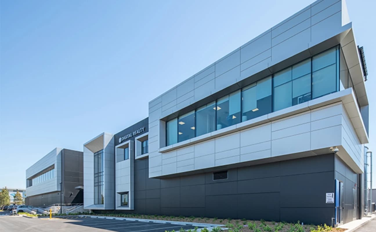 Façade moderne d'un bâtiment Digital Realty avec des panneaux gris clair et foncés et de grandes fenêtres bleutées, sous un ciel clair.