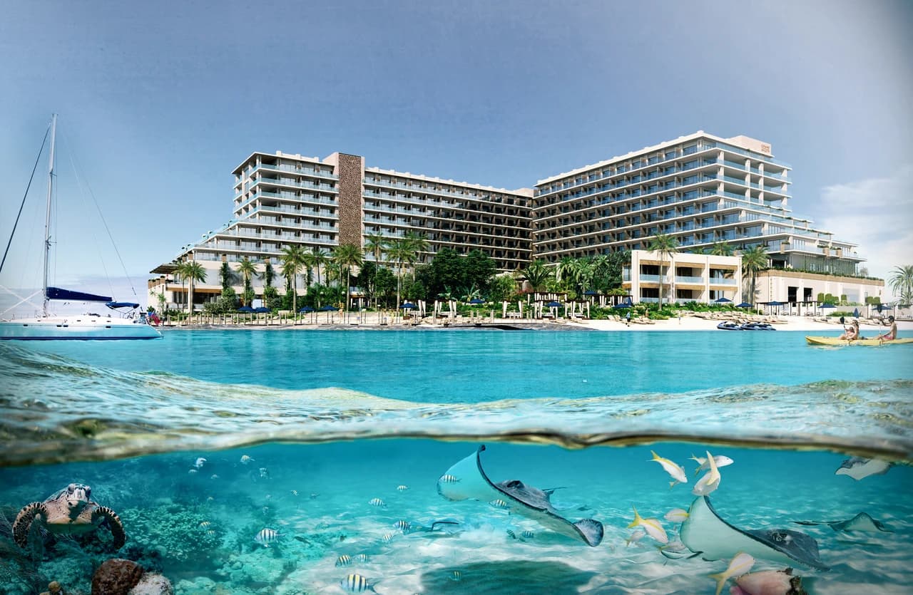 Large luxury hotel complex with a beach and turquoise sea, featuring an underwater view with a turtle, stingrays, and fish, and an above-water view with a hotel, beach, and water activities.