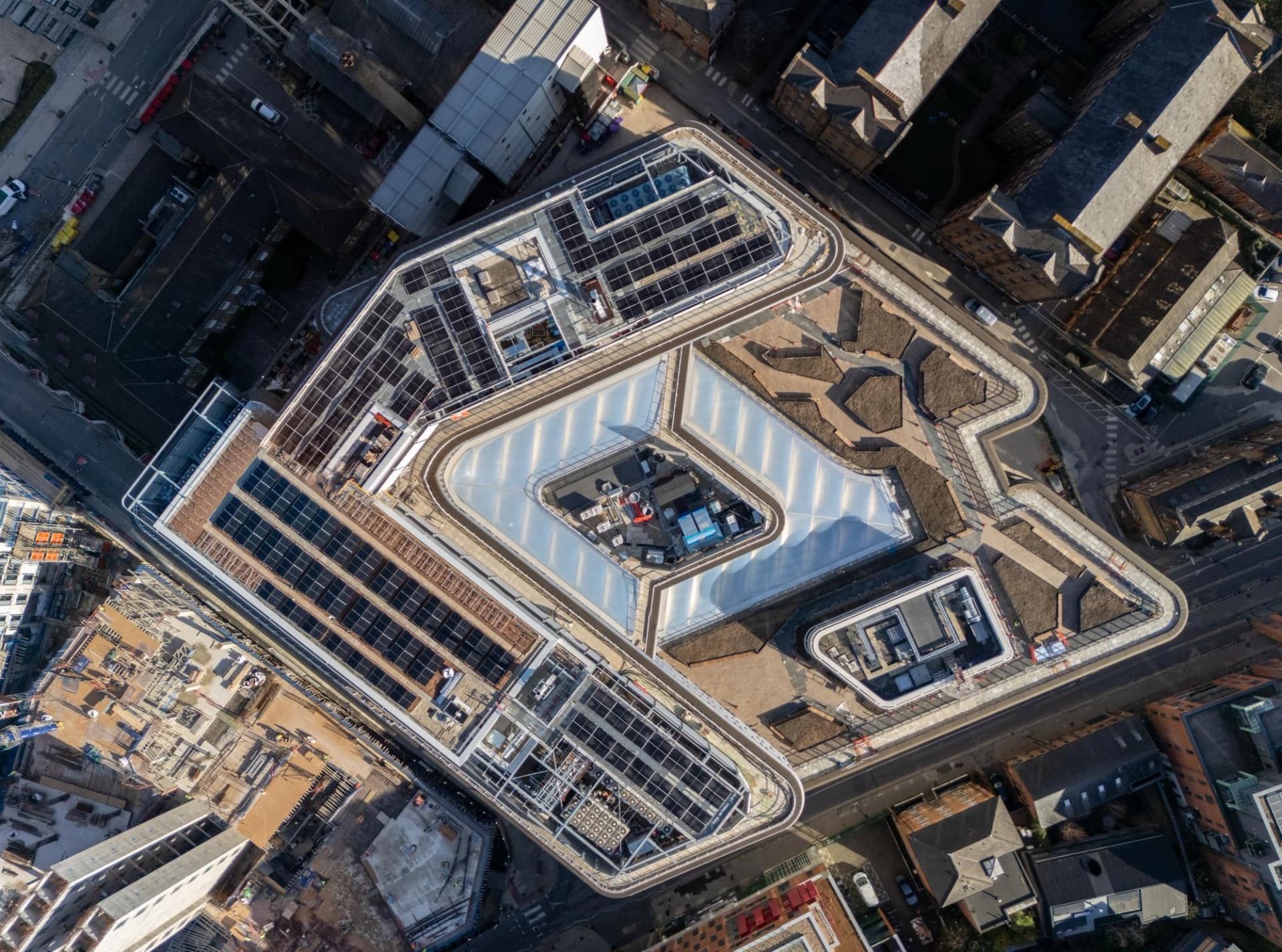 Vue aérienne d'un bâtiment moderne géométrique doté de panneaux solaires et d'une verrière centrale.