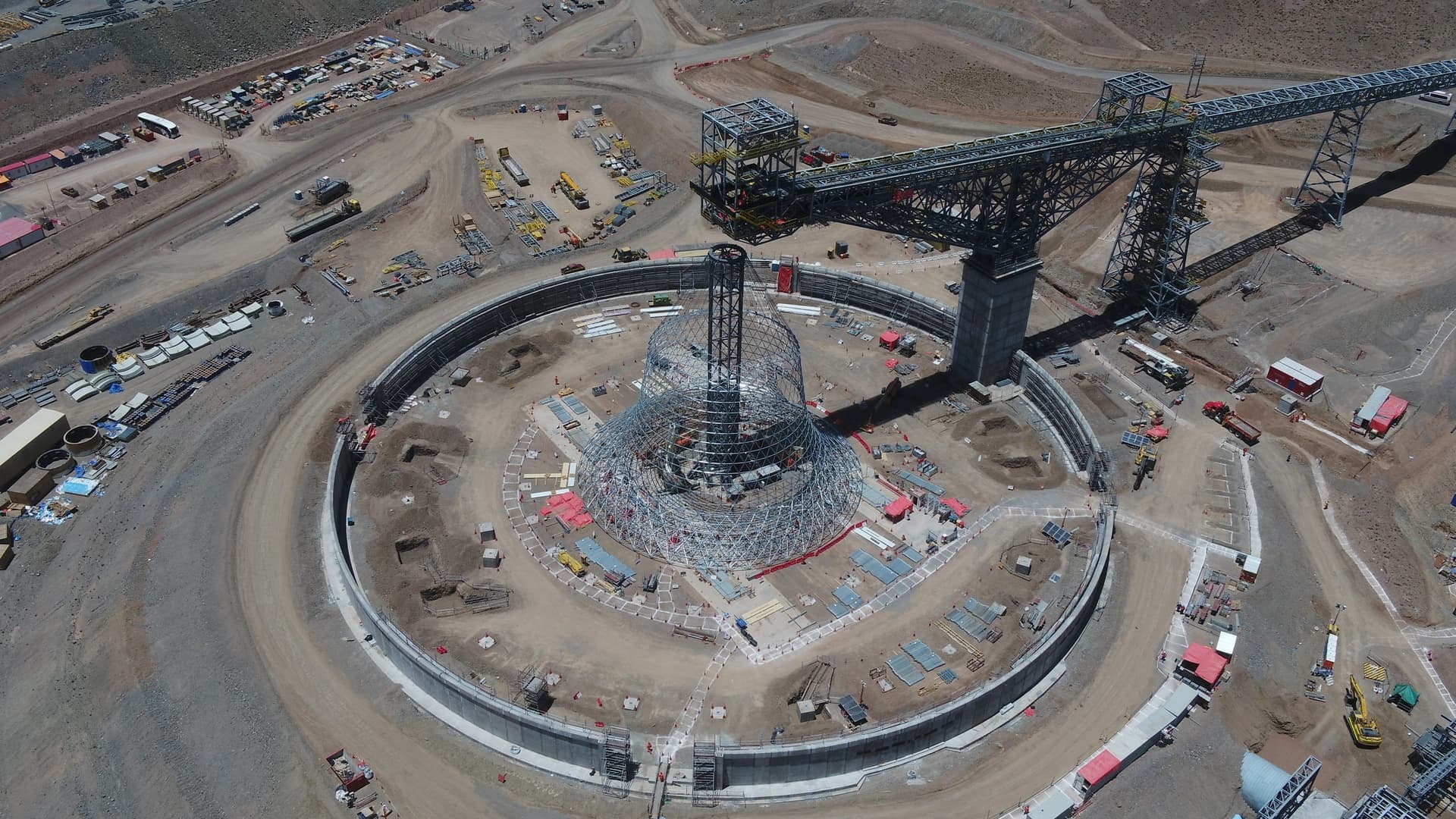 Vue aérienne d'un grand chantier circulaire avec une structure métallique massive et un système de convoyeur industriel.