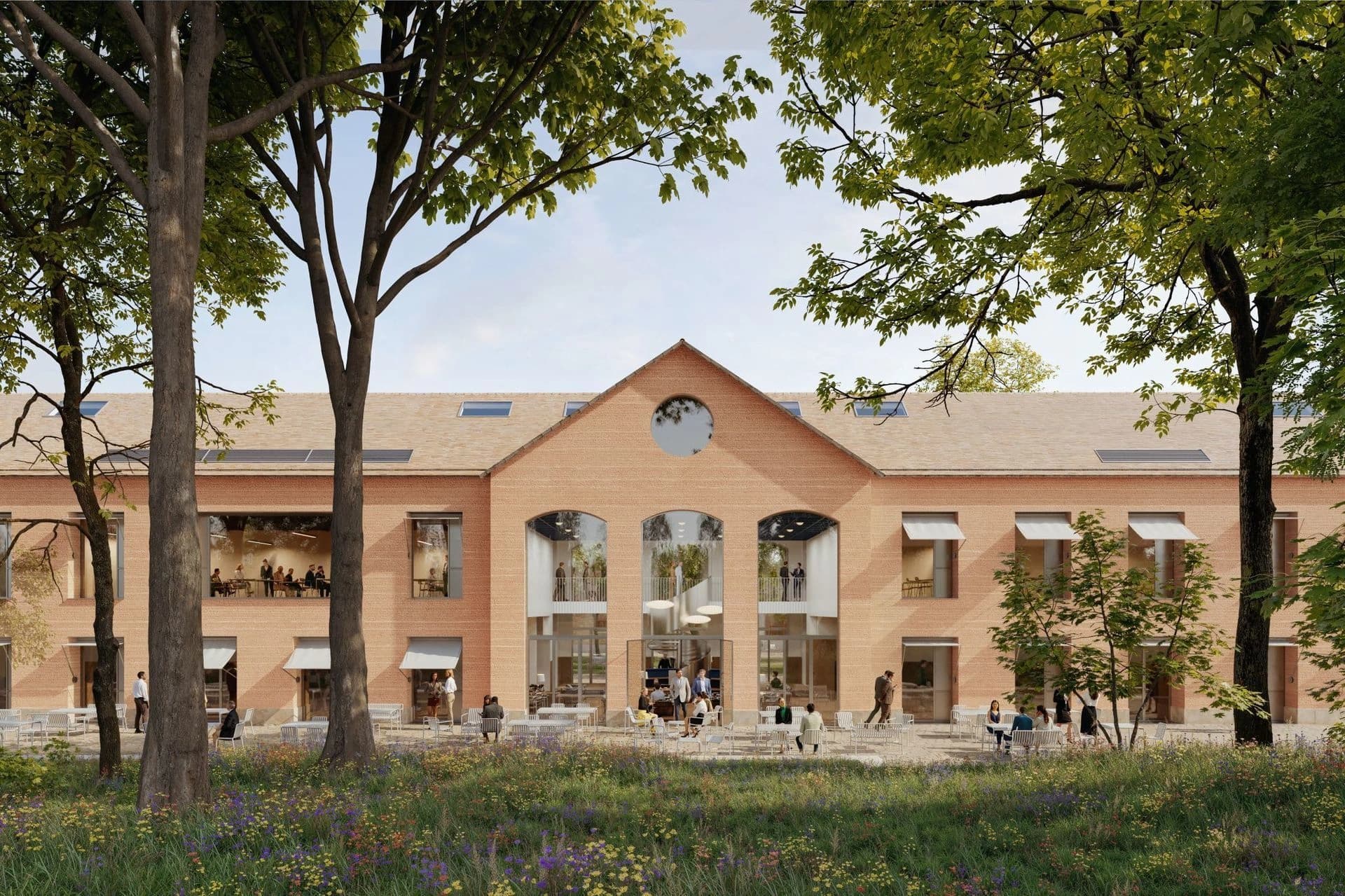Bâtiment moderne en briques aux larges arches vitrées, entouré de verdure avec une terrasse animée.